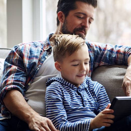 Elternteil schaut gemeinsam mit Kind auf ein Tablet