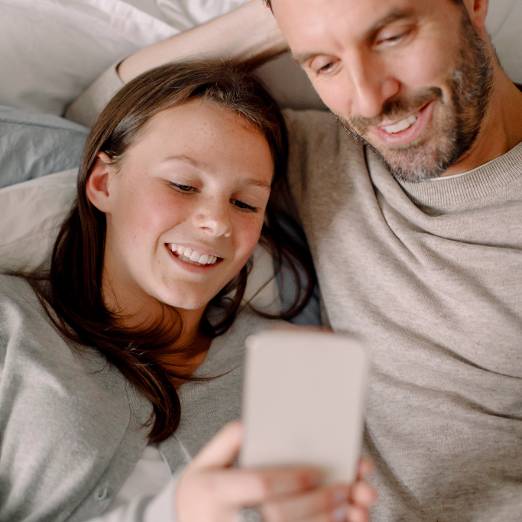 Jugendliches Kind zeigt einem Elternteil etwas auf dem Smartphone